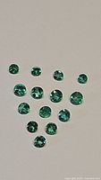 Multiple loose round cut green emerald gemstones arranged on a light surface, showing color and clarity.
