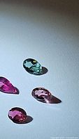 Photo showing four faceted natural tourmaline gemstones in pink and blue hues on a white surface, detailed view of colors and shapes.