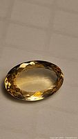 Natural oval cut golden citrine gemstone, faceted, 18.89 carats, shown from top angle in warm light.