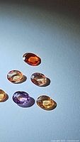 Six oval faceted natural sapphires in exotic colors displayed on a light surface showing their color and clarity under direct light