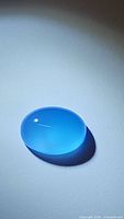 Natural oval cabochon icey blue chalcedony gemstone on white background, illuminated to show translucency and color.