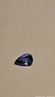 Loose pear-shaped faceted deep purple-blue tanzanite gemstone on neutral background, top view