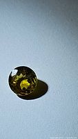 Close-up photo of round, faceted yellow-green sphene gemstone showing high luster and clarity.
