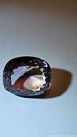 Photo of the 6.67ct natural cushion cut ametrine gemstone showing its faceted surfaces and color variations from different angles under natural light.