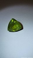 Trillion cut apple green peridot gemstone showing faceting and color under direct light.