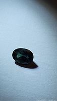 Close-up photo of oval cut natural blue sapphire gemstone on a white surface showing its deep blue-green color and faceting.