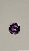 Front-facing photo of natural deep purple round amethyst gemstone showing faceting and clarity.