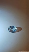 Close-up photo of the oval cut sky blue aquamarine gemstone on a light background showing brilliance and facets.