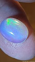 Close-up photo of natural Ethiopian oval cabochon opal showing vivid blue and green color flashes, held between fingers.