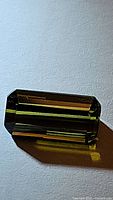 Close-up front view of a natural bright green tourmaline cut in an octagon shape lying on a white surface.