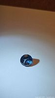 Round faceted natural London Blue Topaz gemstone on white surface showing deep blue color and clarity.