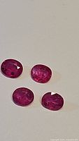 Top view of four oval pink-red rubies showing color and inclusions.