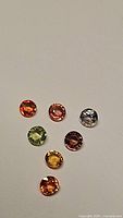 Photo of seven round cut faceted natural sapphires in various rainbow colors, including red, pink, blue, green, yellow, and orange hues.
