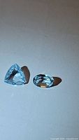 Two loose blue gemstones shown on white background, one trillion cut and one oval cut sky blue topaz.