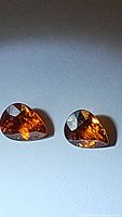 Two pear-cut spessartite garnet gemstones displayed on a neutral background, showing vivid orange color and facet reflections.