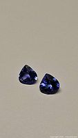 Pair of deep blue-purple pear-shaped tanzanite stones on neutral surface