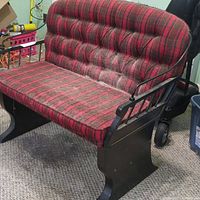 Front left angled view of the carriage bench showing red plaid upholstery and black wood frame with pet hair on the cushions.