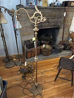 Full view of vintage brass floor lamp standing on wooden floor with fireplace background.