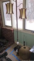 Photo showing mid-century modern floor lamp with hanging resin shades near window, and two metal table lamps on floor beside it.