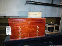 Front view of Thompson humidor with brass handles, pipe stand with black ceramic bowl, and small wooden box on top