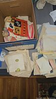 Box containing assorted vintage linens including printed and striped tea towels and other cloths