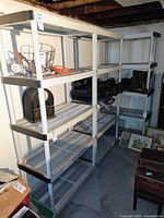 Three heavy-duty plastic shelving units placed side by side in a basement, each with four spacious slatted shelves in light gray and dark gray corners, containing some miscellaneous items and showing signs of use.