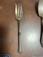 Close-up of a sterling silver fork showing ornate floral pattern on handle and slightly curved tine edge.