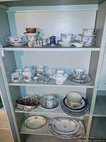 Multiple shelves filled with assorted teacups, saucers, plates, bowls, serving platters, ceramic toast rack, and salt and pepper shakers.