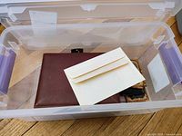 Clear view of the brown leather photo album and included envelope inside a plastic bin