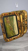 Three vintage metal trays stacked with hand painted hunting scenes and floral gold borders.