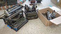 Three items on carpet: Underwood Standard typewriter, Oliver Visible Standard typewriter, and a box with metal typewriter parts.