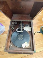 Top-down view of open Victor Talking Machine showing wooden interior, phonograph mechanism with needle, platter with a record, and some loose paper materials.