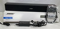Bose Solo TV Speaker, power adapter, optical audio cable in plastic bag, and original box.