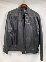 Front view of black men's leather jacket with zipped pockets and stand collar, displayed on wooden branded hanger.