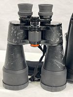 Front view of Celestron Ultima 9x63 binoculars showing black body with scattering of exterior scuffs and marks. Rubber eyecups and central adjustment knob visible.