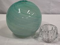 Photo showing the blue-green swirl spherical glass vase next to one of the three full leaf crystal vases, displaying size and design details.