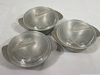 Three vintage small round au gratin dishes with hammered aluminum texture and glass shark fin lids arranged on a white surface.