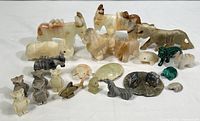 Wide view showing full set of 22 polished stone animal carvings of various types and sizes on white background.