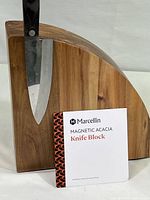 Front view of magnetic acacia wood knife block with a serrated knife magnetically attached and brand informational card visible.