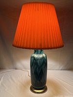 Full view of the Mid Century Modern blue ceramic lamp with orange pleated shade illuminated, showing overall size and form.