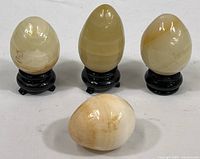 Group of four polished mineral eggs, three on black stands, arranged on white surface