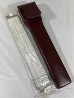 New Teledyne Post 13-inch slide rule in original sealed plastic wrap next to brown leather carry pouch with belt strap.