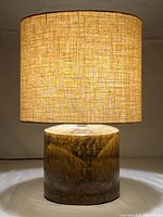 Front view of the table lamp lit to show illumination through the beige fabric shade and the brown glazed ceramic base.