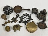 Lot of vintage brass and cast iron decorative items including flower frog, incense burners, figurines, souvenir ashtray and Buddha figure shown together on table.