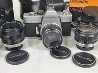 Full view of Minolta SRT 101 camera with three lenses positioned in front, leather case and flash visible in background