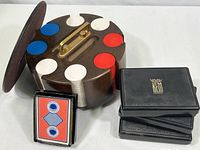 Overall view of revolving hardwood poker chip stand with lid, stacked poker chips in red, white, and blue, and three black KEM playing card cases along with a partial nudie card deck.
