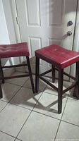 Two red faux leather barstools with dark wood legs placed on tiled floor near a door.