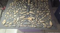 Full display of approximately 150 lithic artifacts including flint arrowheads, chert points, ground stones on backing