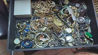 Top view of drawer filled with assorted costume jewelry and wristwatches showing mixed types and colors