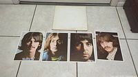 The four individual color photographic portrait prints of The Beatles members placed in front of the album cover